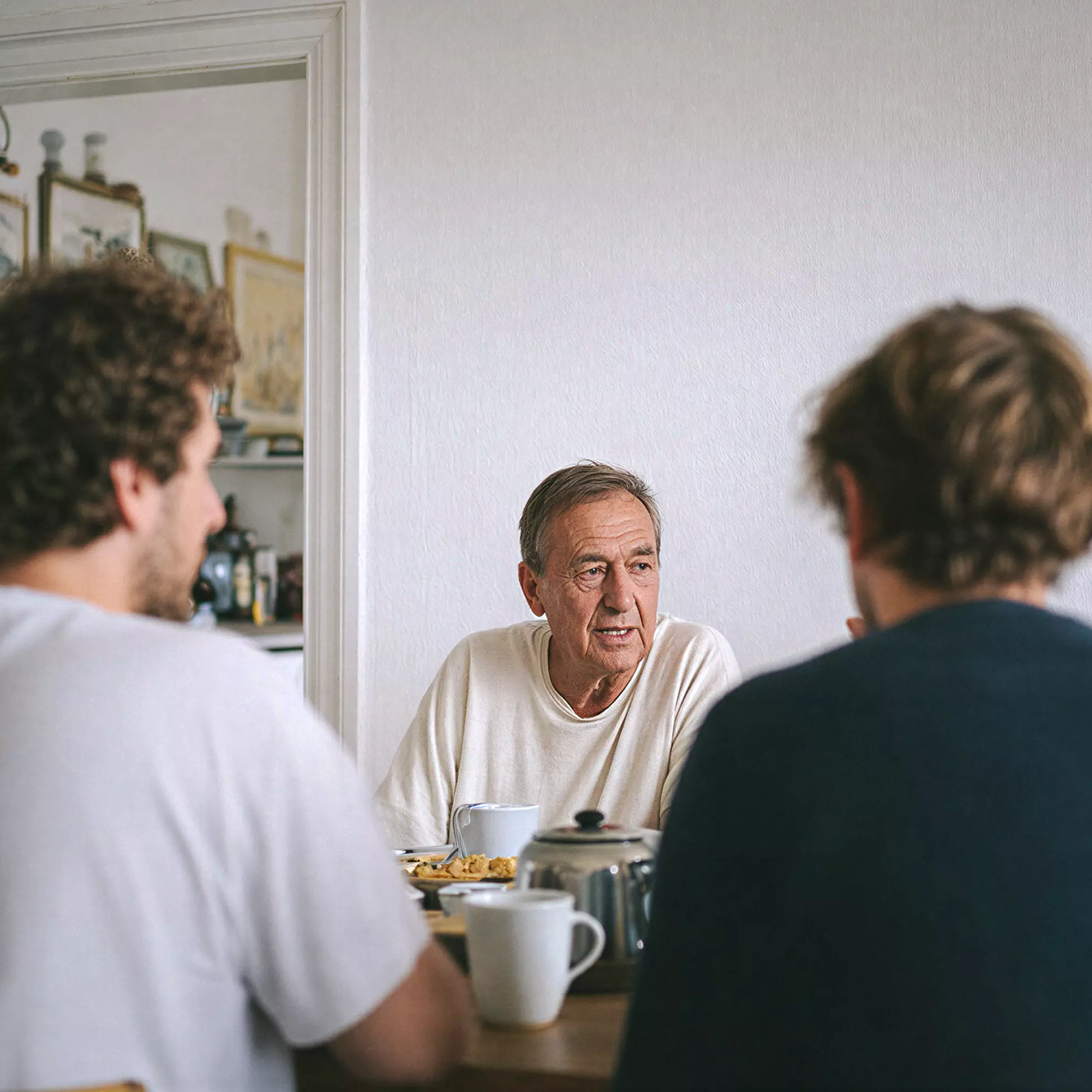 Old man sitting for breakfast at the table facing two young men