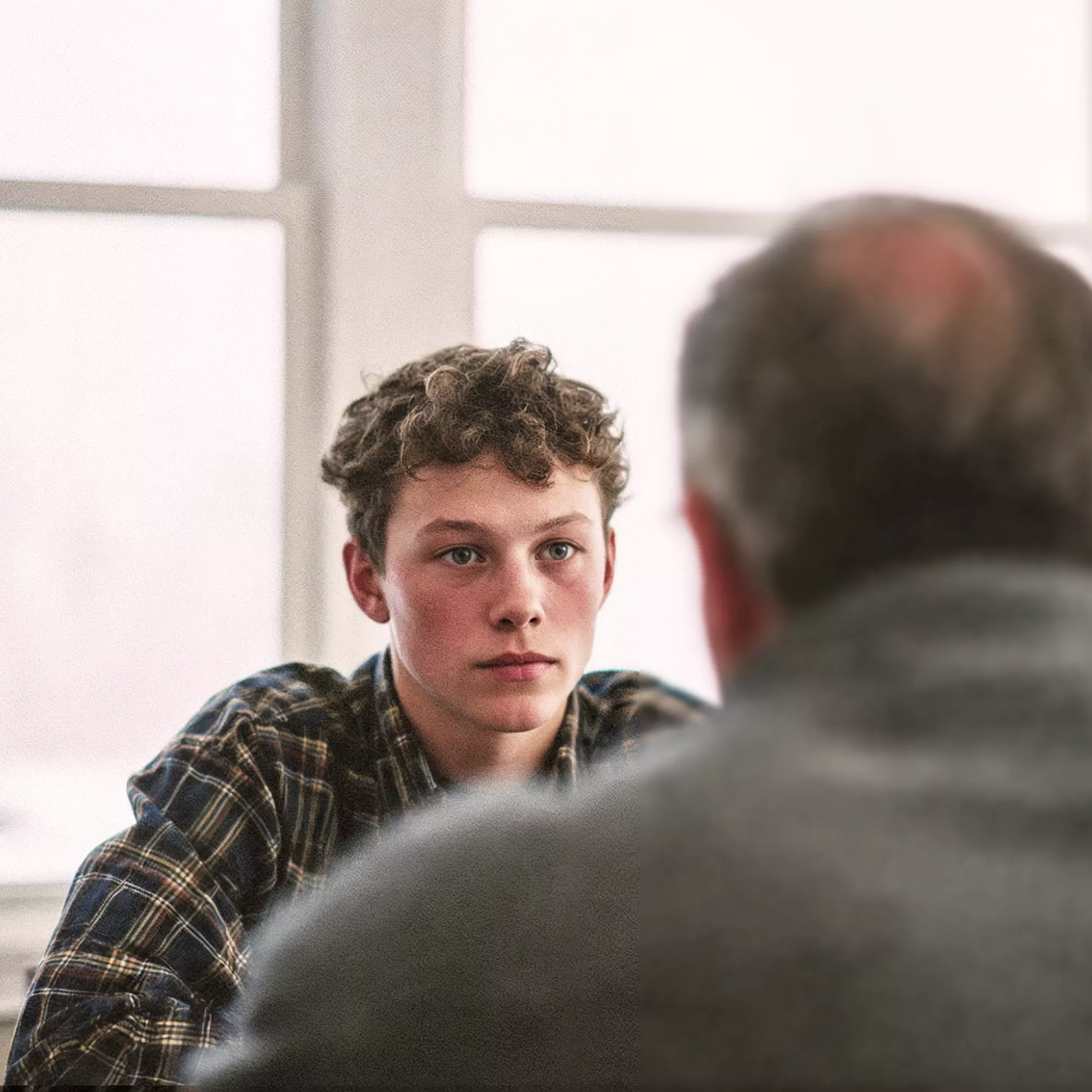 Yound man with curly hair sitting in front of an older one and facing him