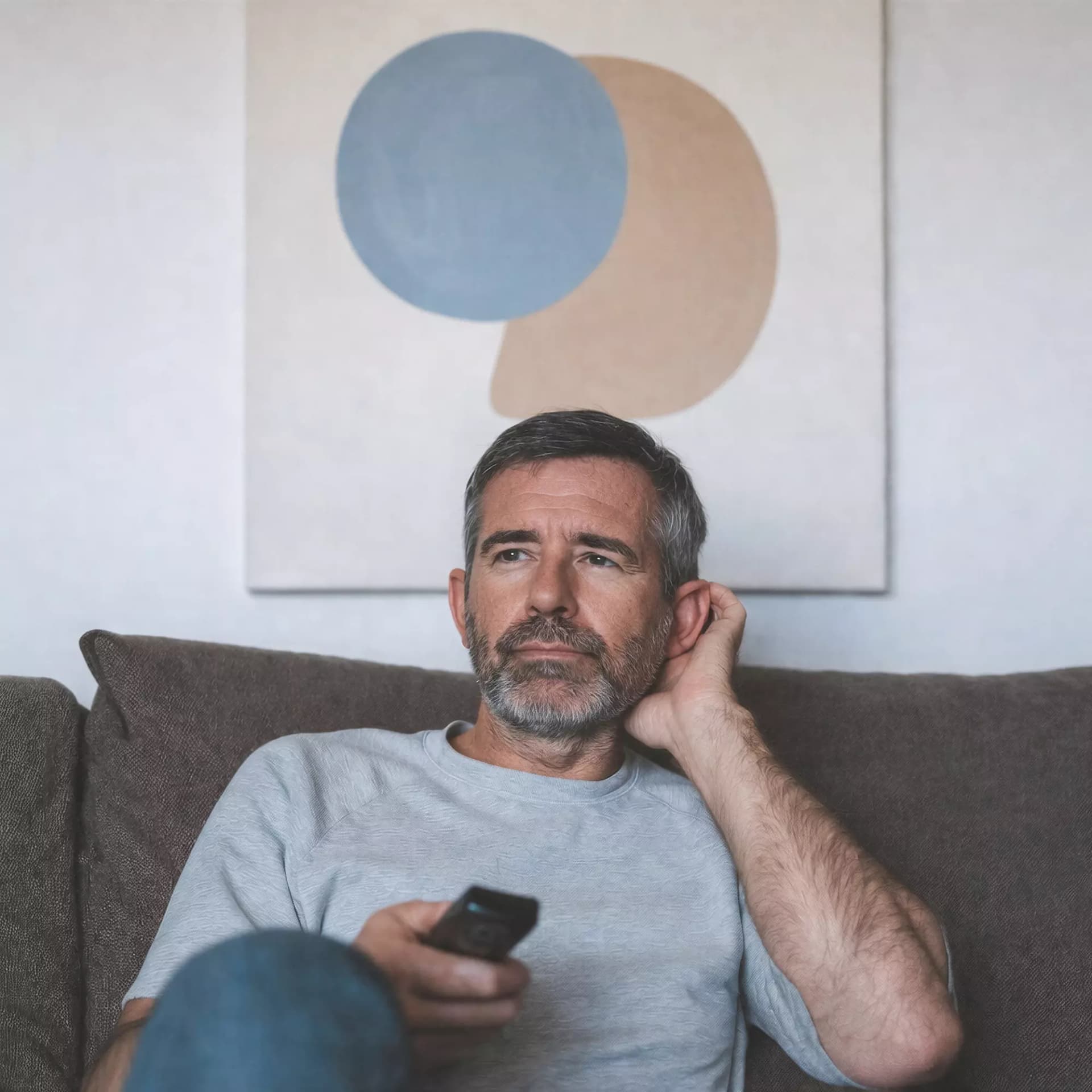 Man sitting on the couch holding his ear with a tv controller in his right hand