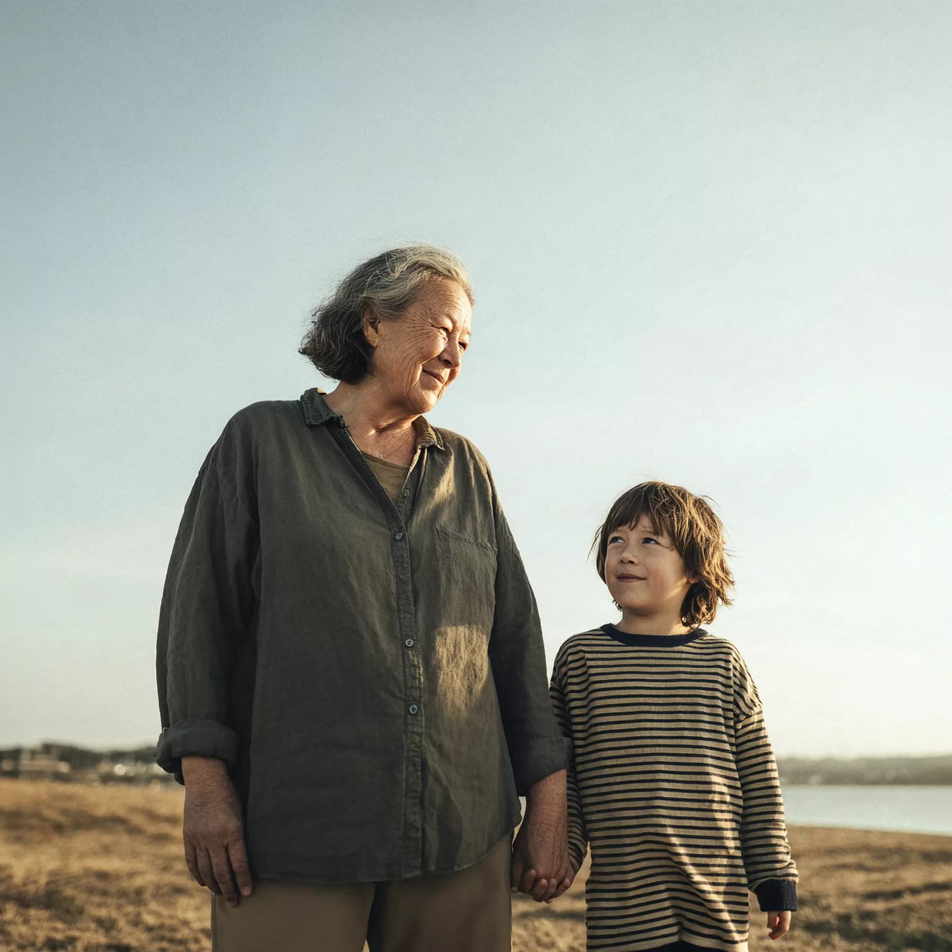 Older woman with grey hair holding hands with a young kid close to the beach