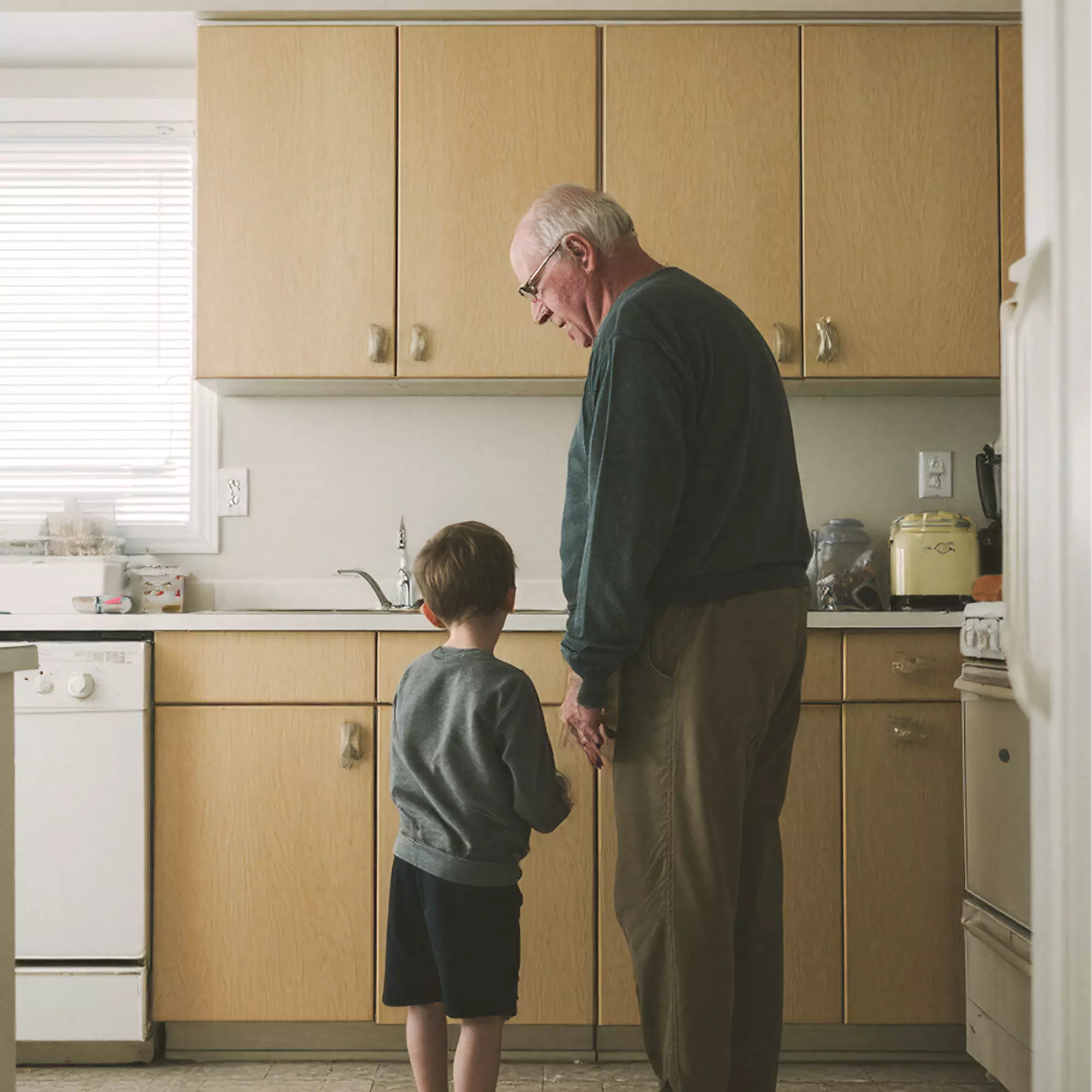 Old man standing in front of the kitchen counter with a small boy