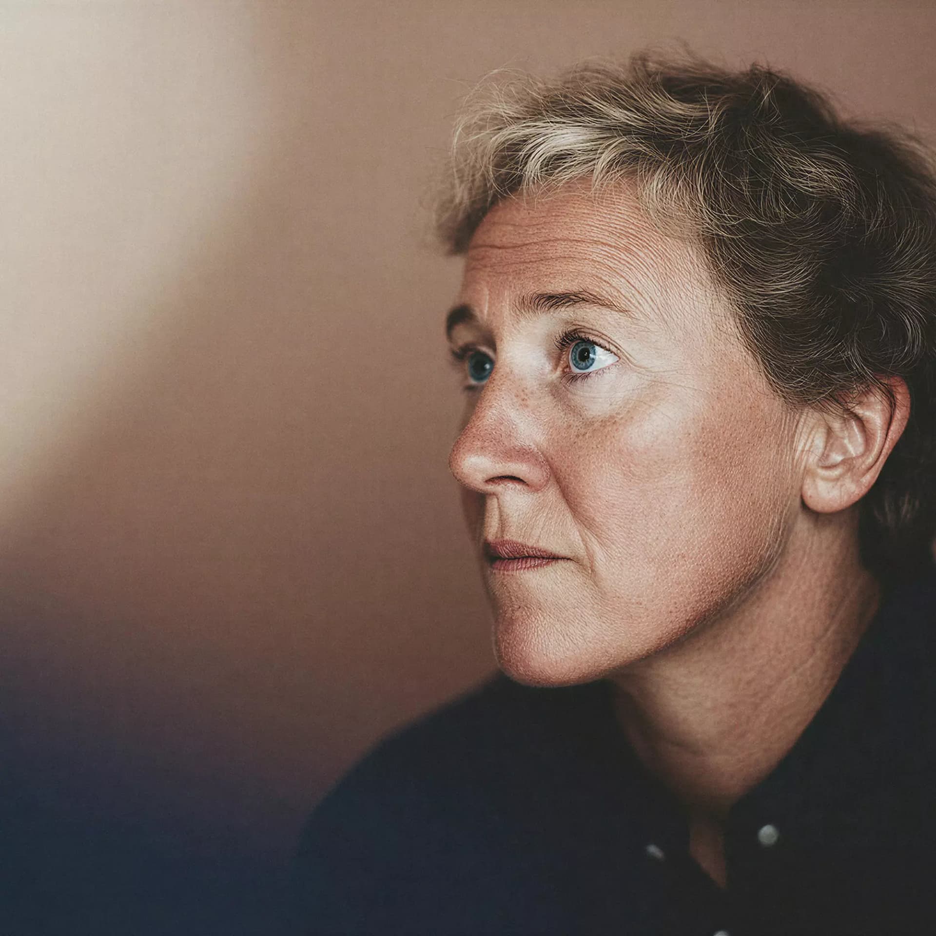 Woman with short hair and green eyes on a warm brown background
